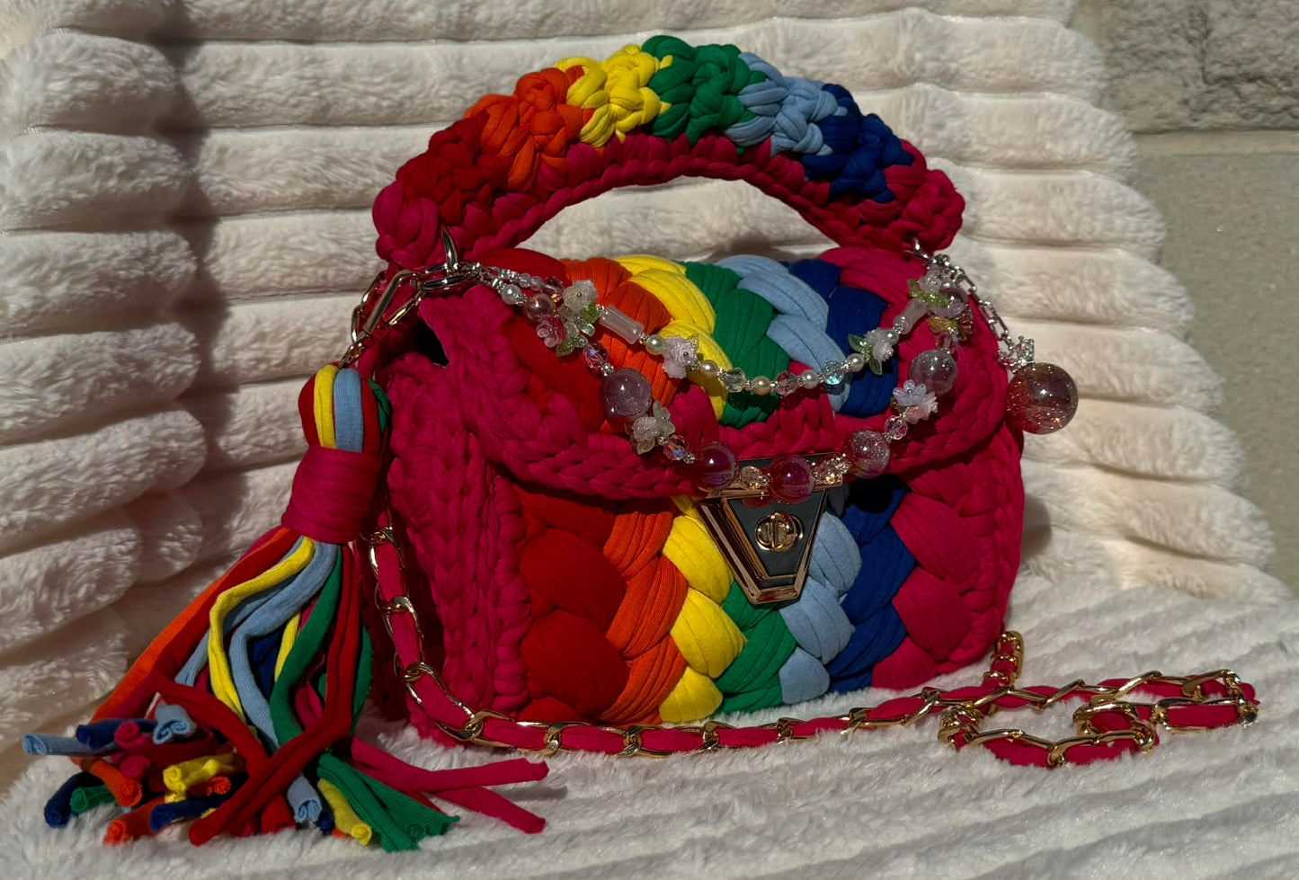 Front of the bag in full sun: Colorful Crochet woven handbag with rainbow pattern and beautiful decorative keychain on a white surface. Rainbow pattern includes: Hot Pink, Red, Orange, Yellow, Green, Light Blue, and Dark Blue.