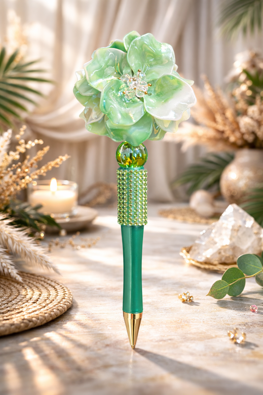 Green decorative bling pen with flower top on a table with decorative elements in the background.