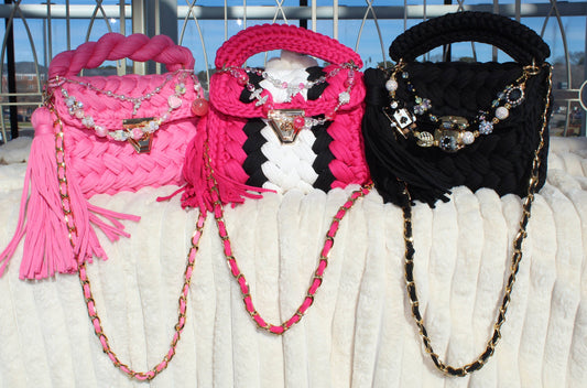 Three Crochet handbags in Pink, Black, and Mixed Colors with decorative keychains sitting on a White textured surface.