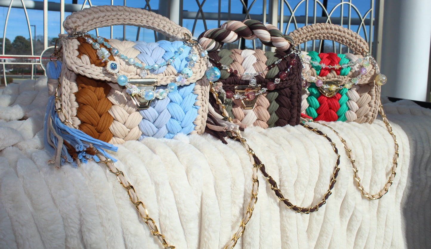 Three colorful handbags with chain straps and beautiful keychains sitting on a textured surface.