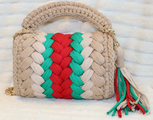 Back view of bag in natural lighting: Shades of Green, Red, Tan, and Nude with tassel sitting on a white tectured surface and background.