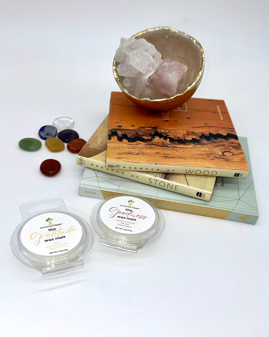 Two wax melts on a white surface with books, a crystal bowl, and stones in the background.