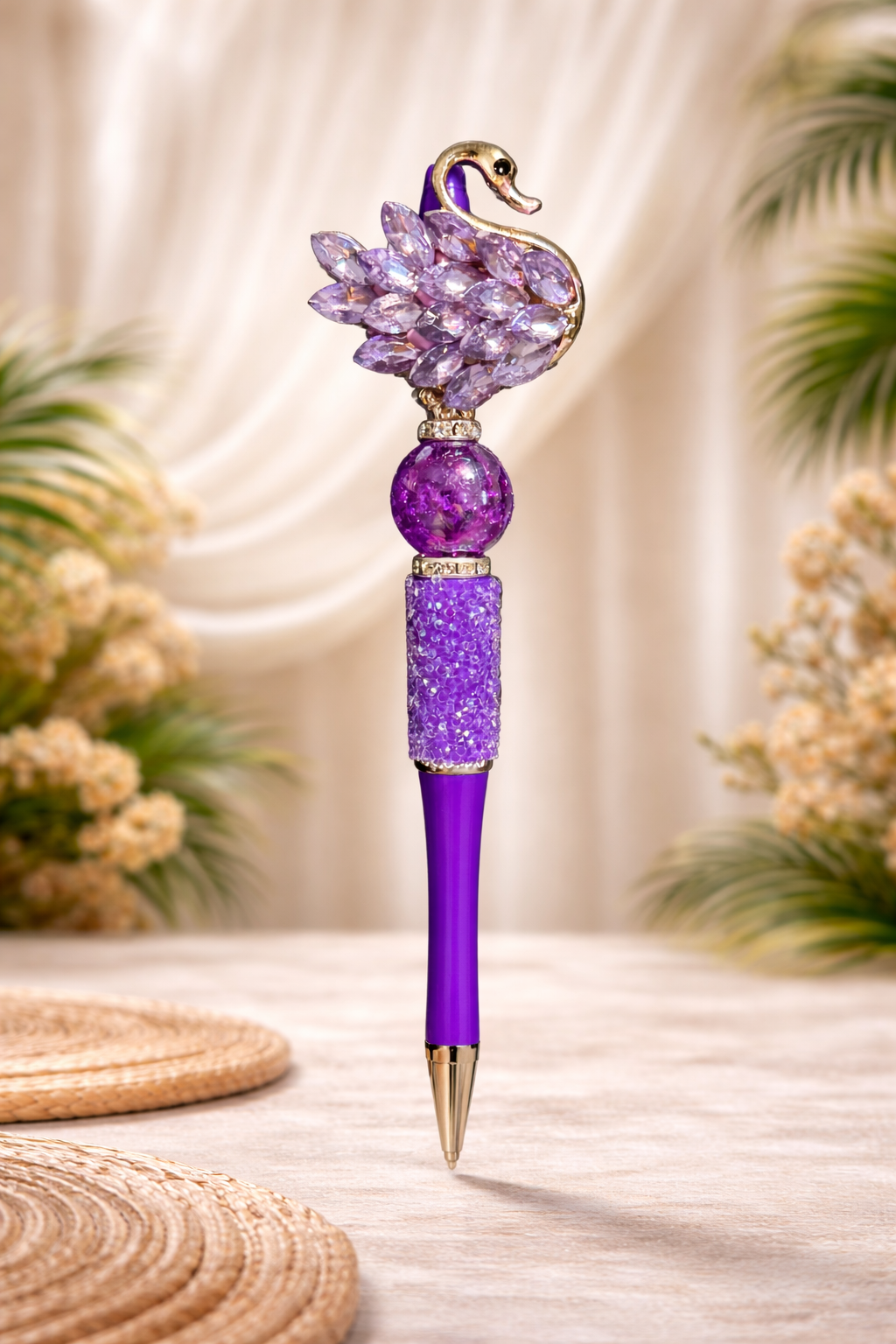 Decorative purple swan bling pen on a smooth rustic surface with plants and placemats in the bakground.