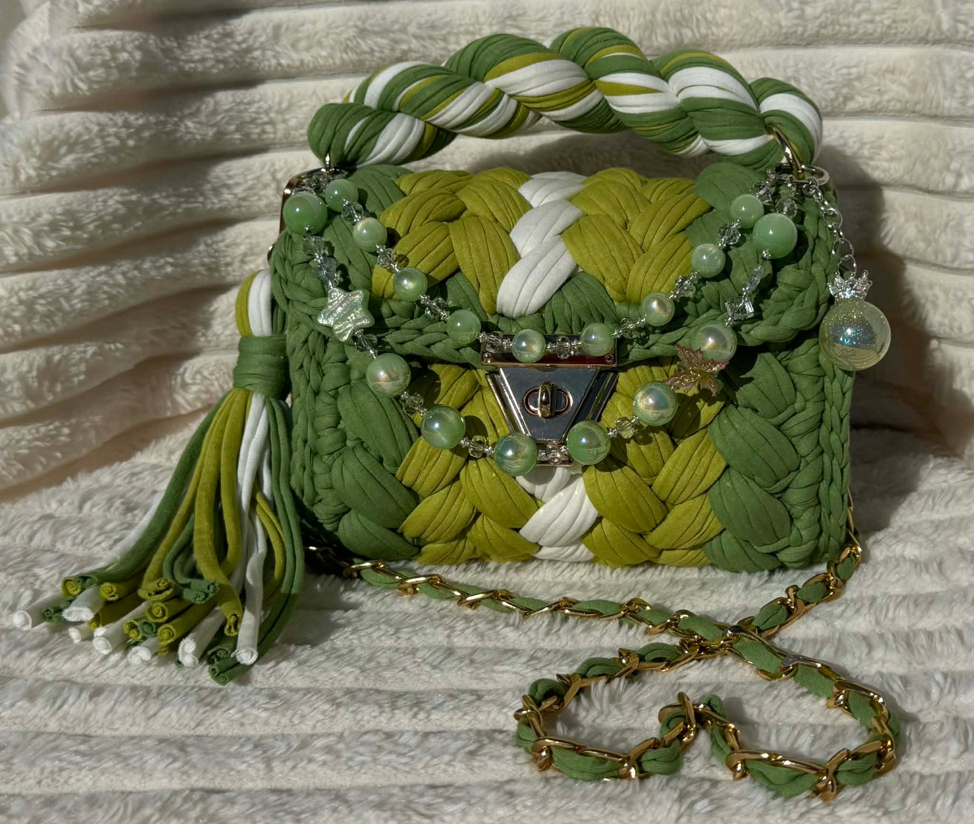 Front view of the bag in full sun: Shades of Green & White crochet woven texture with decorative keychain, sitting on a textured surface.