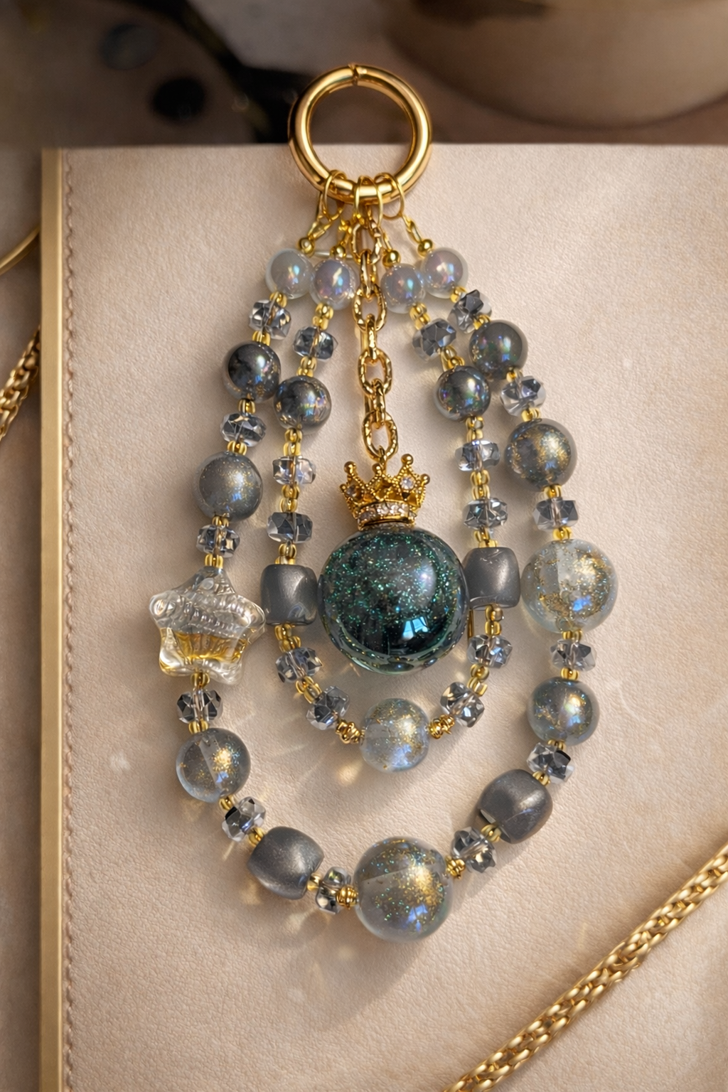 Decorative keychain with shimmering silver beads and gold accents on a soft, beige background with gold trim. 
