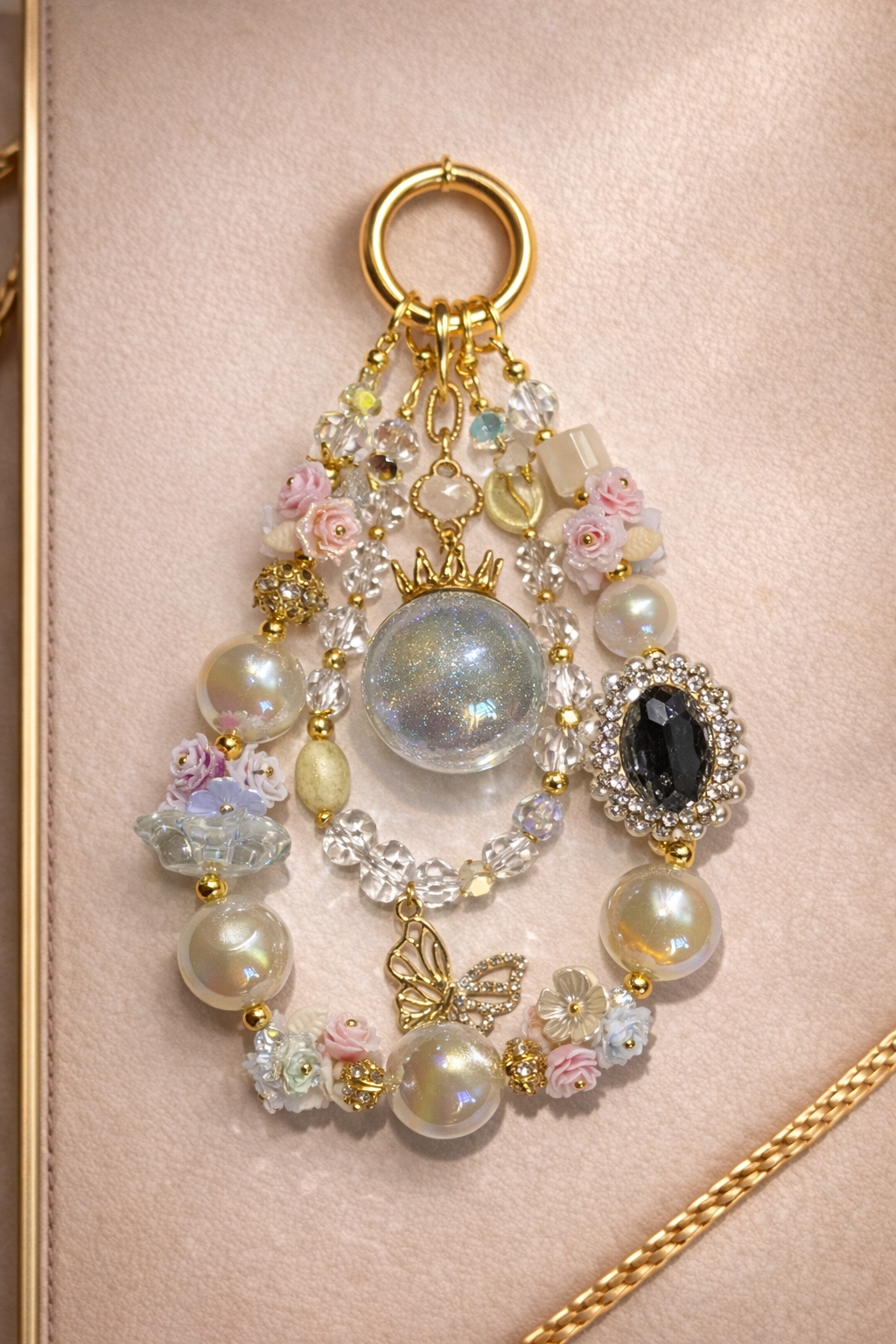 Decorative keychain with white pearl beads, floral accents, and a butterfly pendant on a soft, beige background with gold trim. 