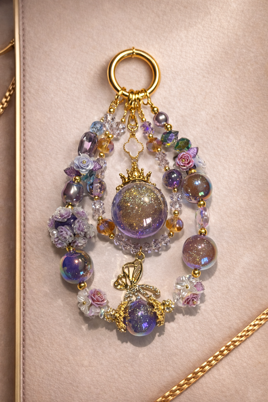 Decorative keychain with shimmering lavender & lilac beads and a butterfly pendant on a soft, beige surface with gold trim. 