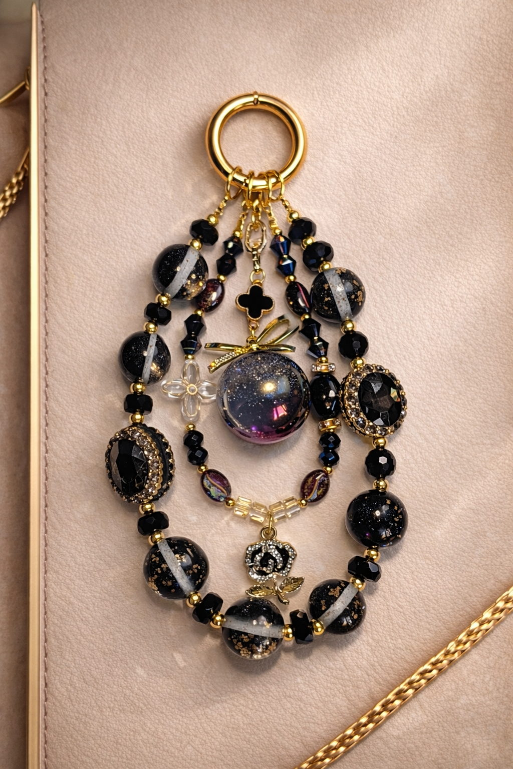 Decorative gold keychain with black and white stripe beads and a black rose pendant on a soft, beige background with gold trim. 