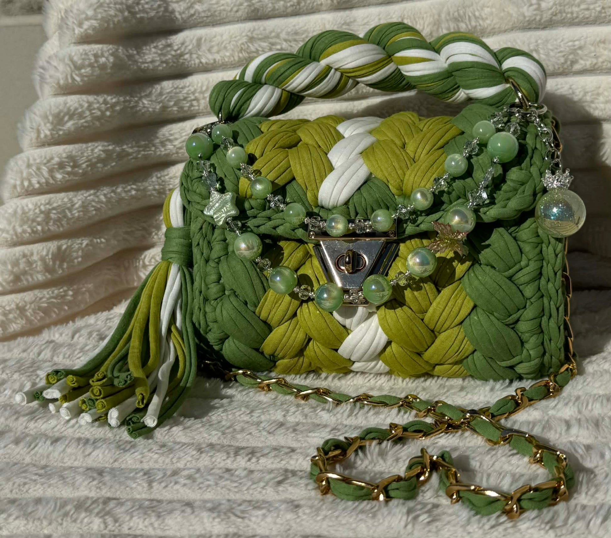 Front view of the bag in full sun: Shades of Green & White crochet woven texture with decorative keychain, sitting on a textured surface.