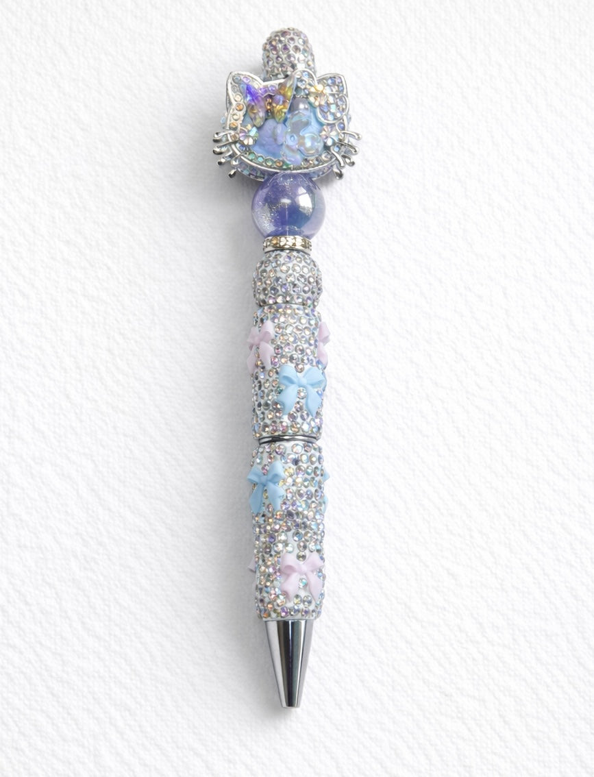 Blue decorative kitty-cat pen with gemstone-like beads on a white cardstock background