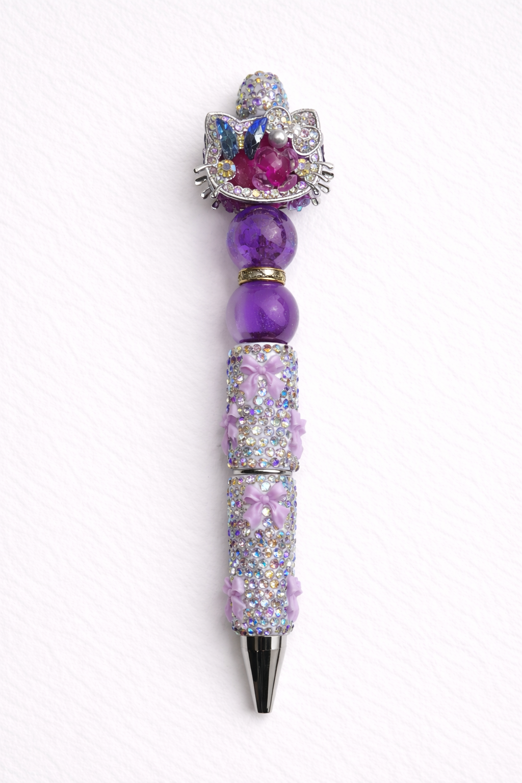 Purple decorative kitty-cat pen with gemstone-like beads on a white cardstock background