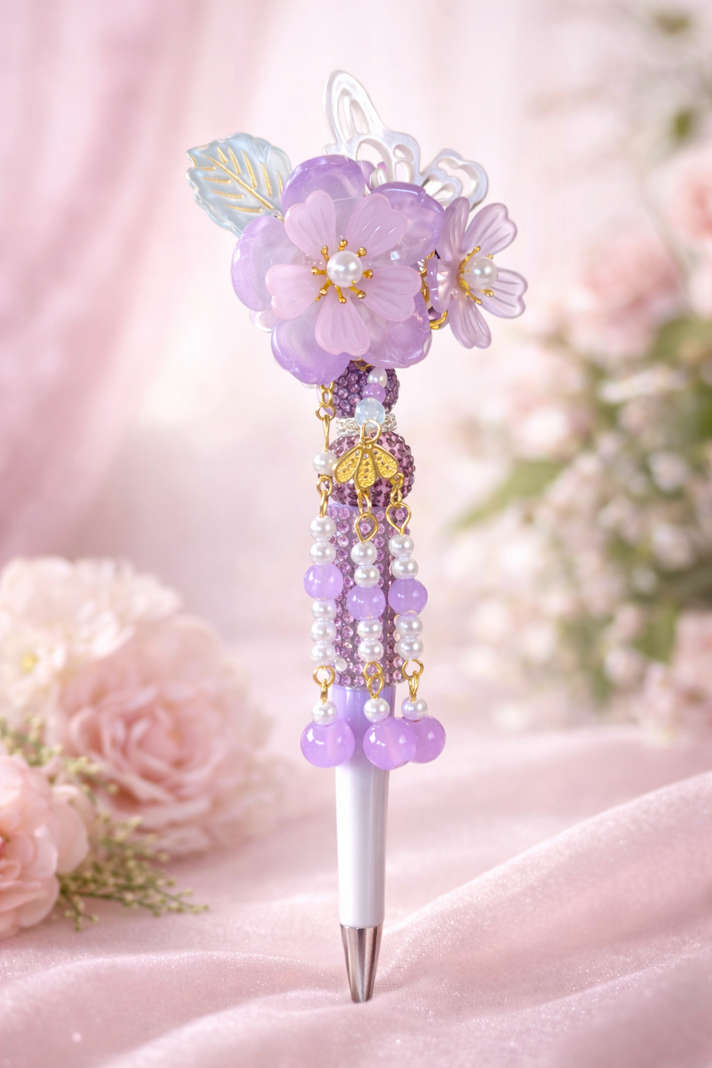 Decorative flower pen with beaded chains and butterfly accent on a soft pink background