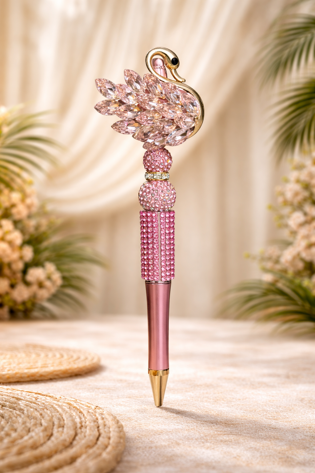 Decorative pink swan bling pen on a smooth rustic surface with plants and placemats in the bakground. 