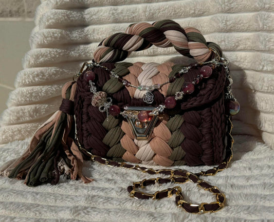 Front view of bag in full sun: Colorful woven Crochet handbag (Brown, Tan, Moss Green, and Beige) with tassel and beautiful shimmering keychain sitting on a white, textured surface. 