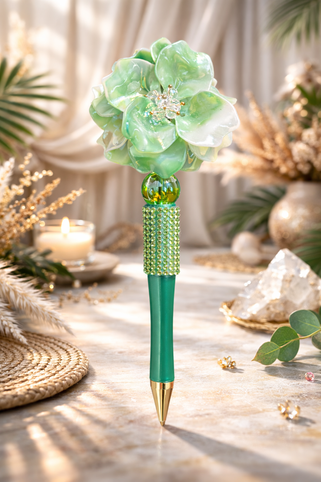Green decorative bling pen with flower top on a table with decorative elements in the background. 