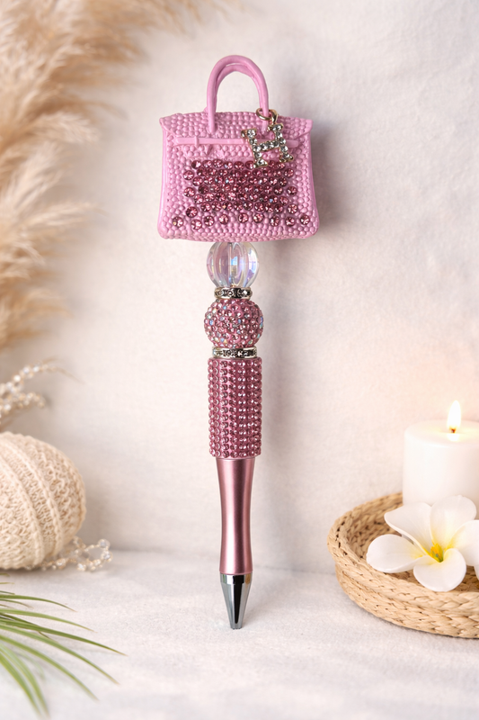 Pink decorative pen with a small H-handbag on top, on a soft background