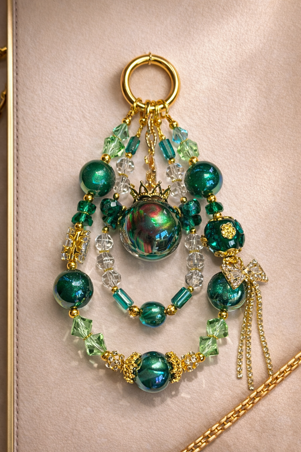 Decorative keychain with green and gold accented beads on a soft, beige background with gold trim. 