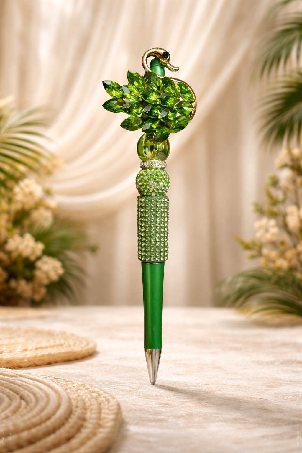 Decorative green swan bling pen on a smooth rustic surface with plants and placemats in the bakground. 