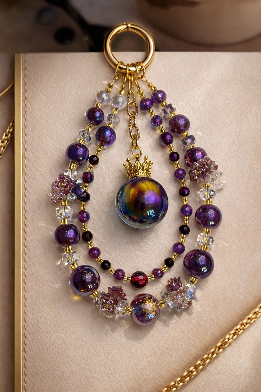 Decorative keychain with deep purple beads and small floral accents on a soft, beige surface with gold trim. 