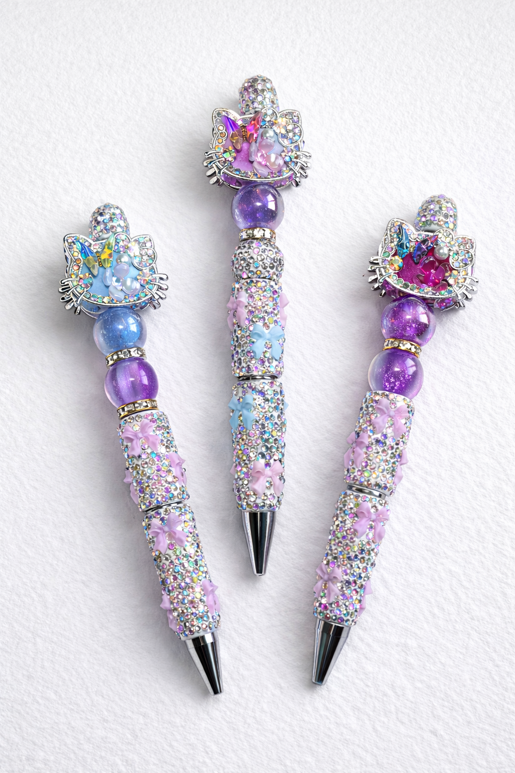 Three decorative kitty-cat pens with gemstone-like beads on a white cardstock background