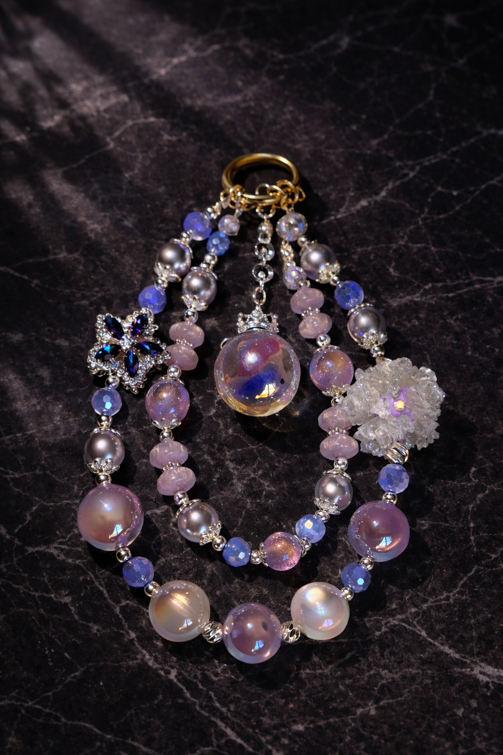 Decorative purple and lavender keychain with a large flower charm, a small star bead, and shimmering beads on a dark textured marble background. 