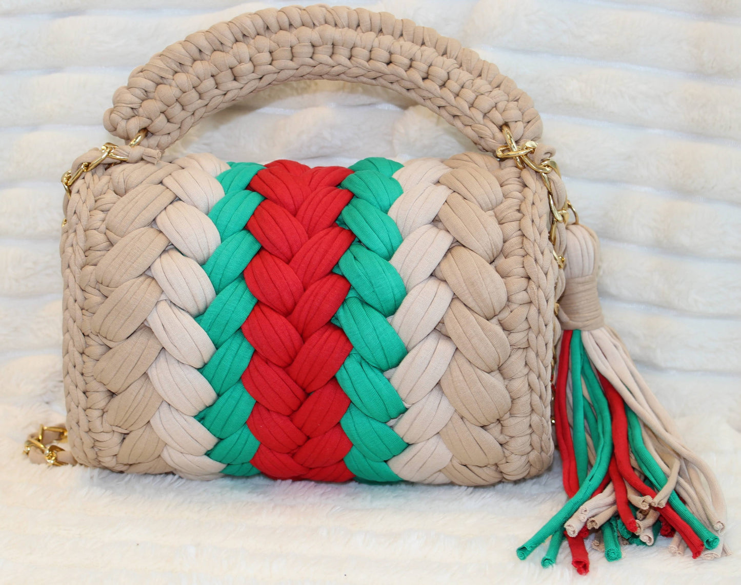 Back view of bag in natural lighting: Shades of Green, Red, Tan, and Nude with tassel sitting on a white tectured surface and background. 