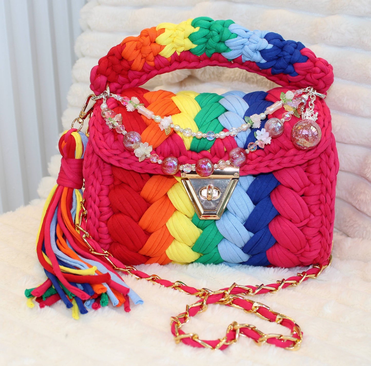 Front of the bag in natural lighting: Colorful Crochet woven handbag with rainbow pattern and beautiful decorative keychain on a white surface. Rainbow pattern includes: Hot Pink, Red, Orange, Yellow, Green, Light Blue, and Dark Blue. 