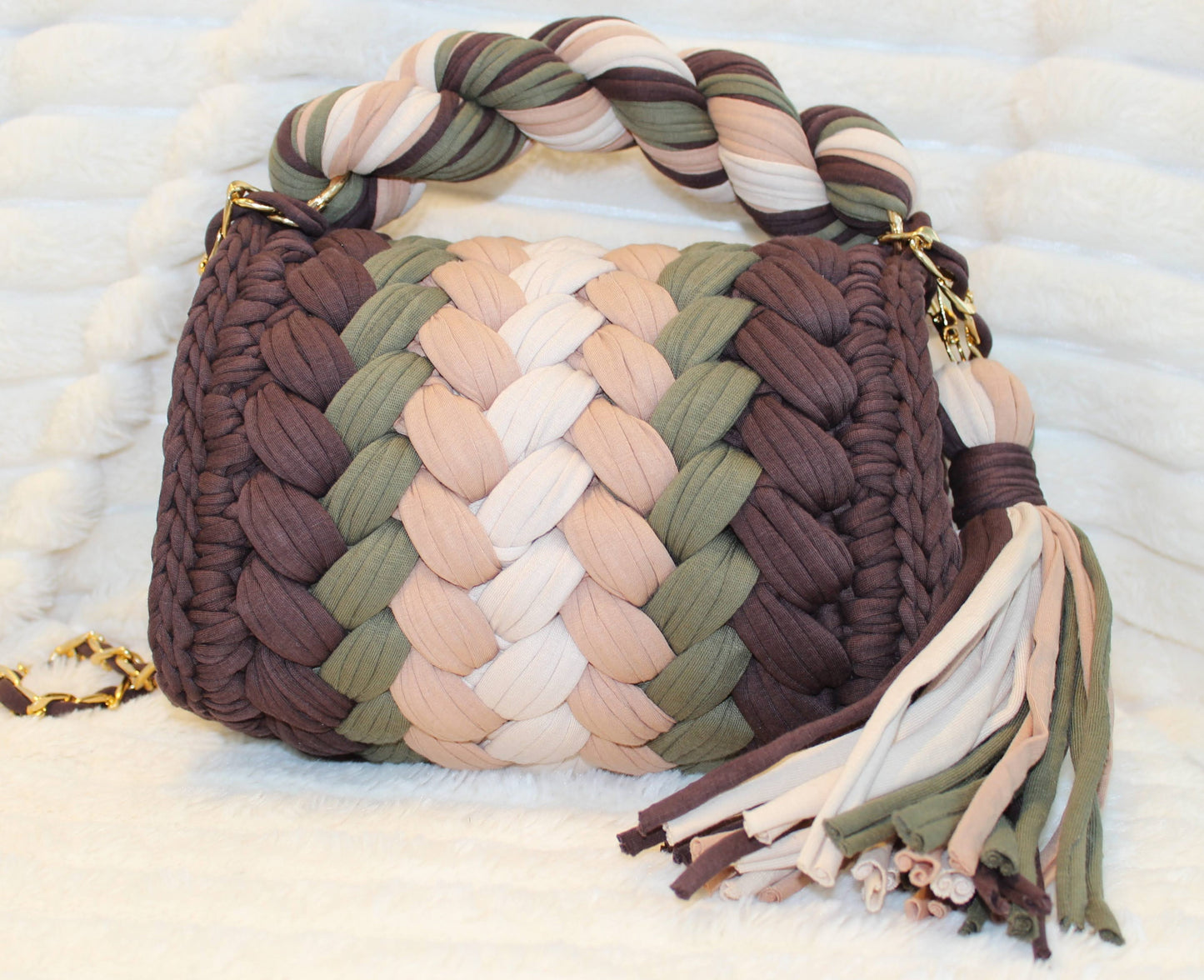 Back view of bag in natural lighting: Colorful woven Crochet handbag (Brown, Tan, Moss Green, and Beige) with tassel sitting on a white, textured surface. 