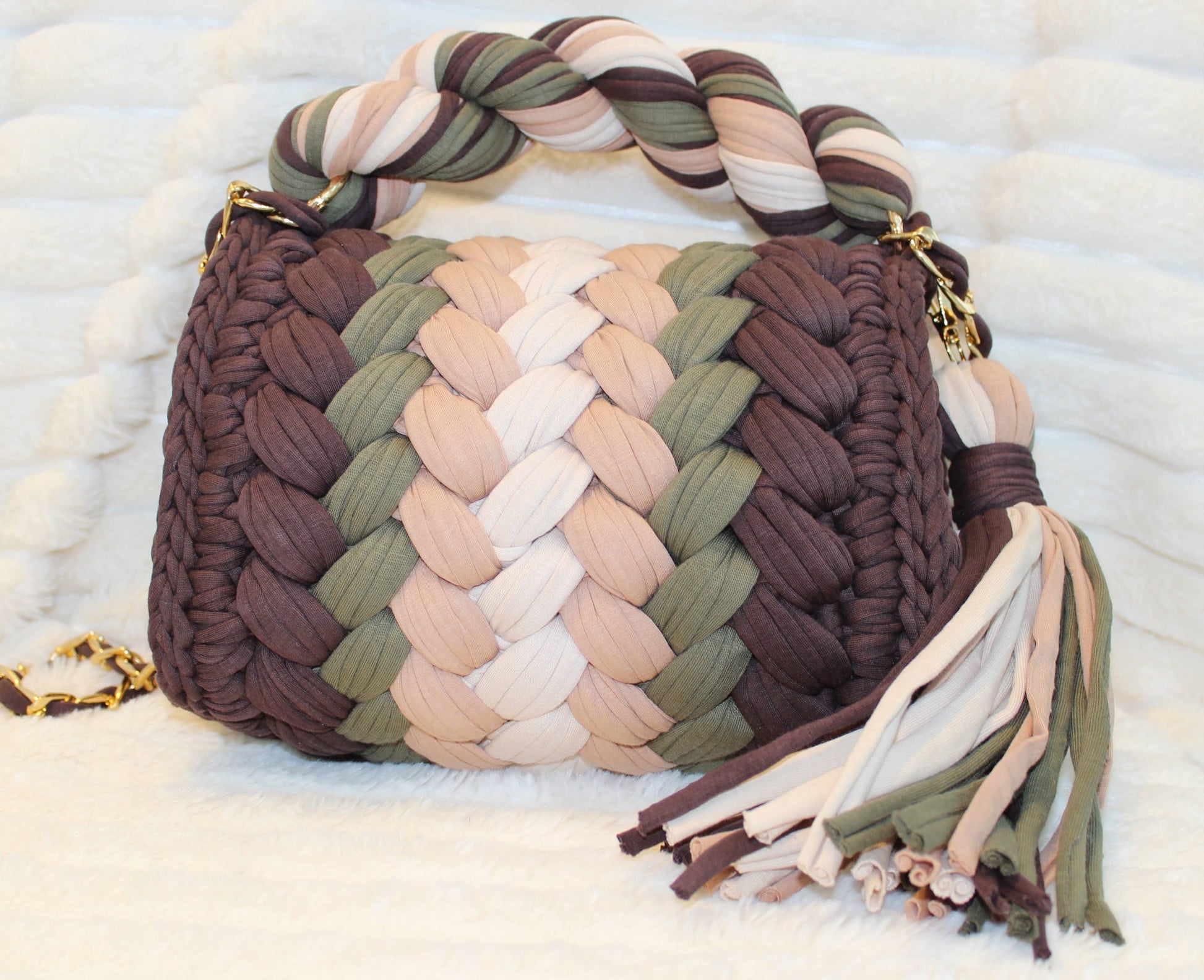 Back view of bag in natural lighting: Colorful woven Crochet handbag (Brown, Tan, Moss Green, and Beige) with tassel sitting on a white, textured surface. 