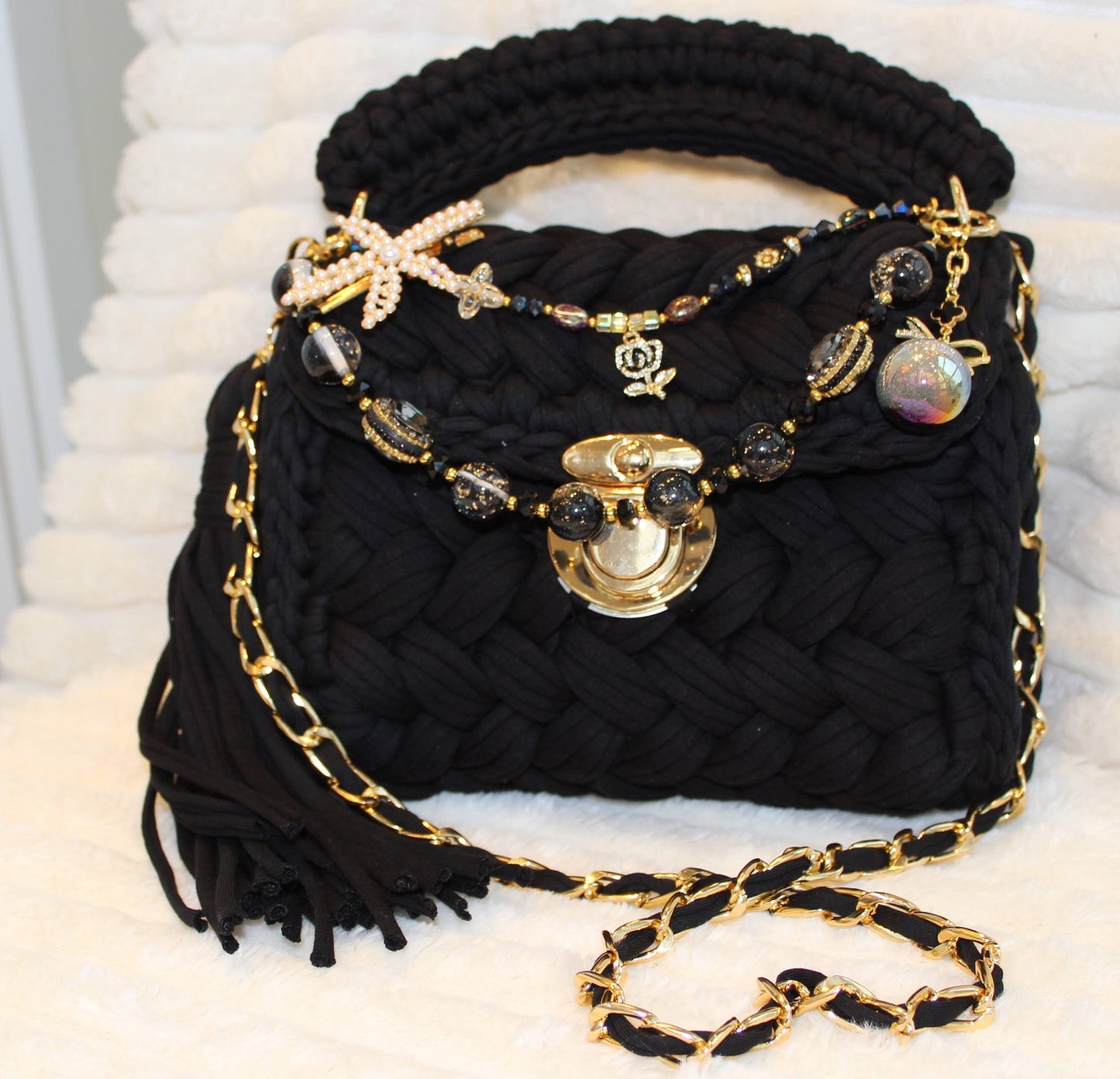 Front view of the bag: Black Crochet woven handbag with black tassel, beautiful keychain and decorative elements on a White textured background. 