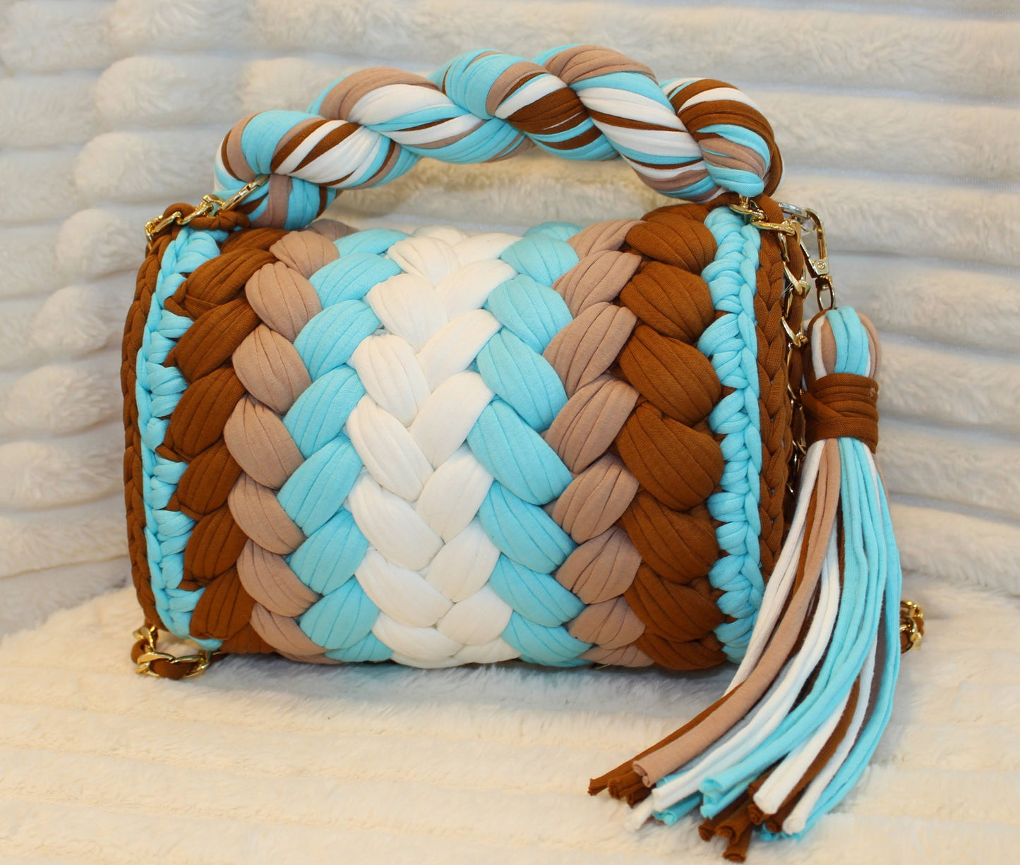 Back view of bag in natural lighting: Colorful woven Crochet handbag (White, Brown, Turquoise, & Milk Chocolate) with tassel sitting on a white, textured surface. 