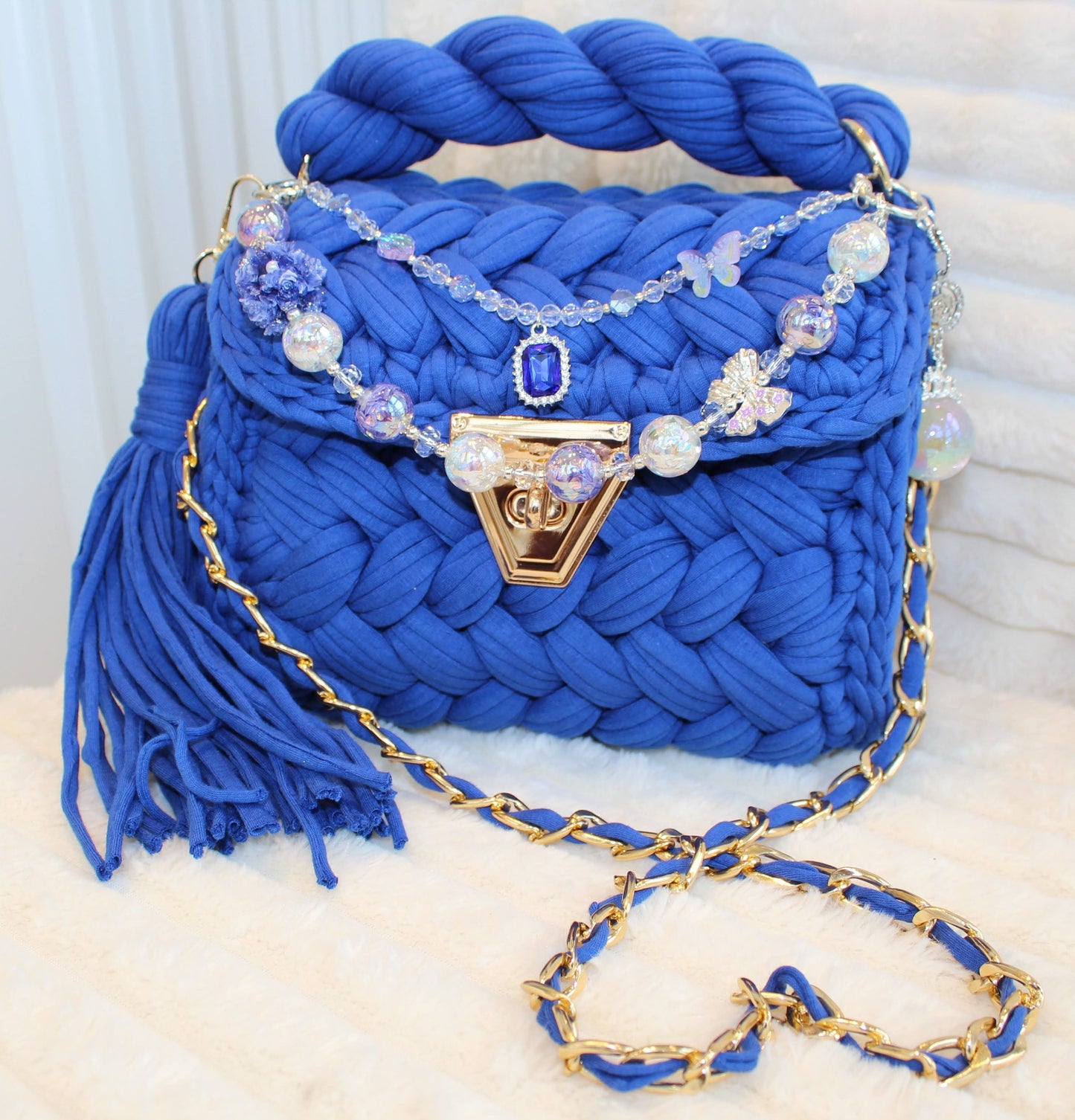 Front View of the bag in natural lighting: Royal/Indigo Blue Crochet woven handbag with decorative keychain chain and tassel on a textured White background surface.