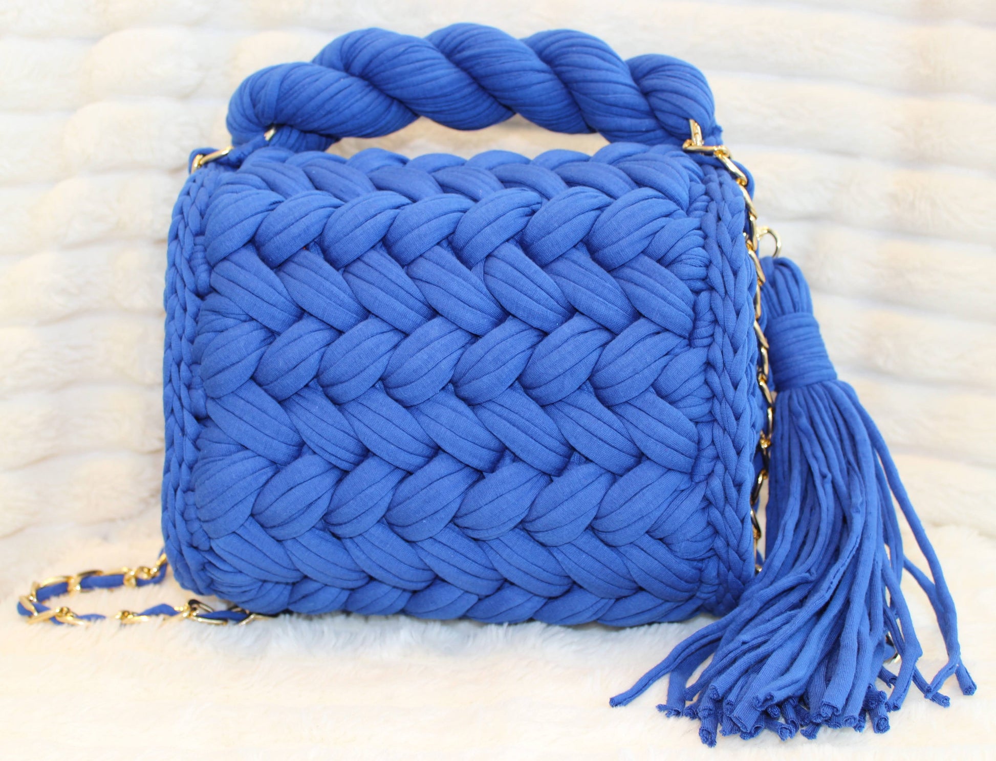 Back of the bag in natural lighting: Royal/Indigo Blue Crochet woven handbag with tassel on a textured White background surface.