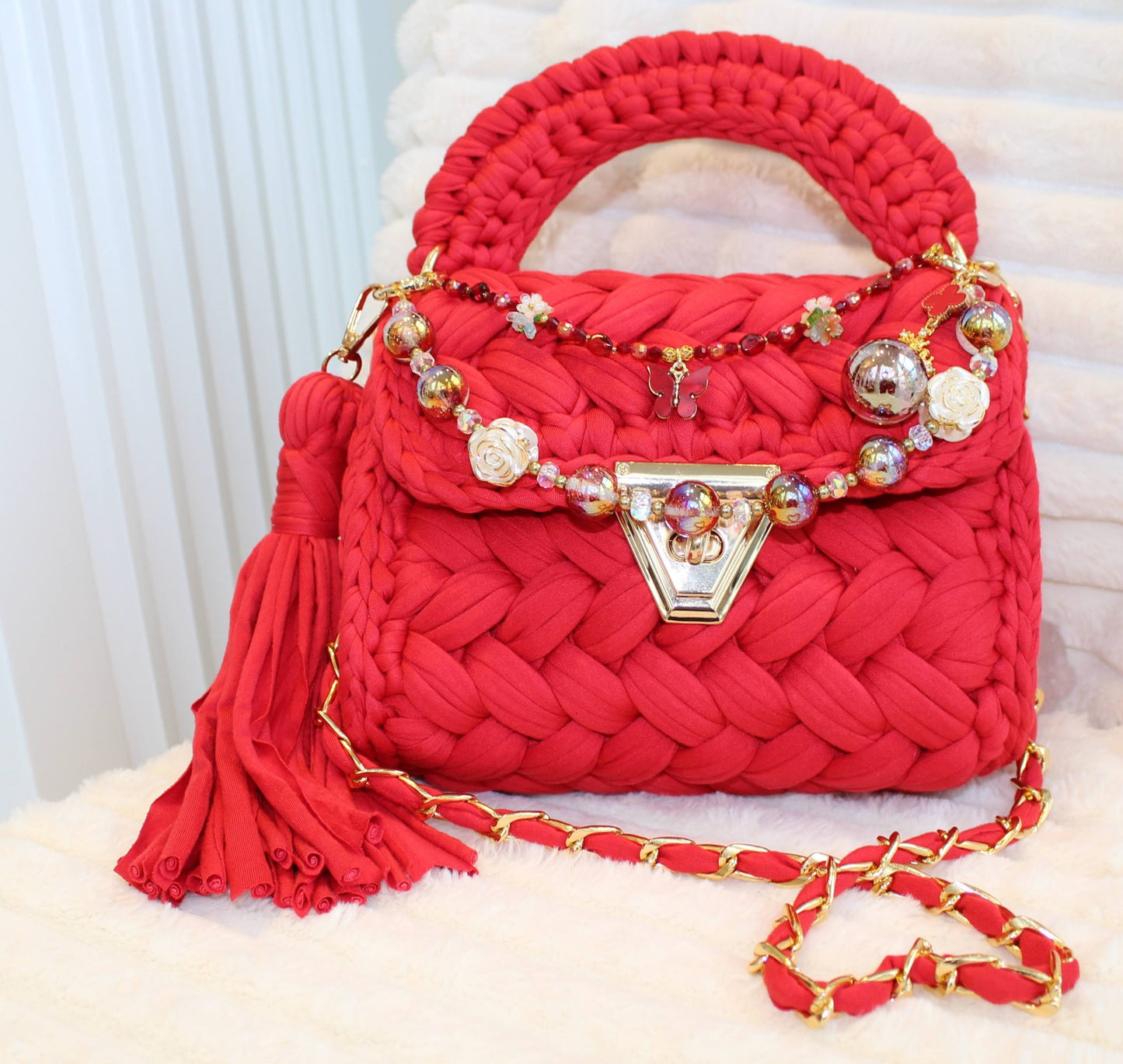 Front view in natural lighting: Red woven Crochet handbag with decorative keychain chain and tassel on a textured White background. 