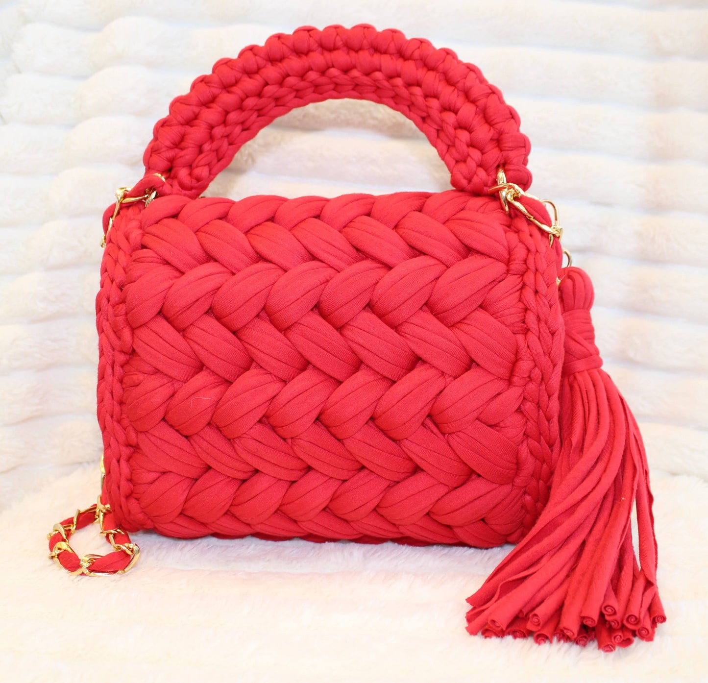 Back view in full sun: Red woven Crochet handbag with tassel on a textured White background. 