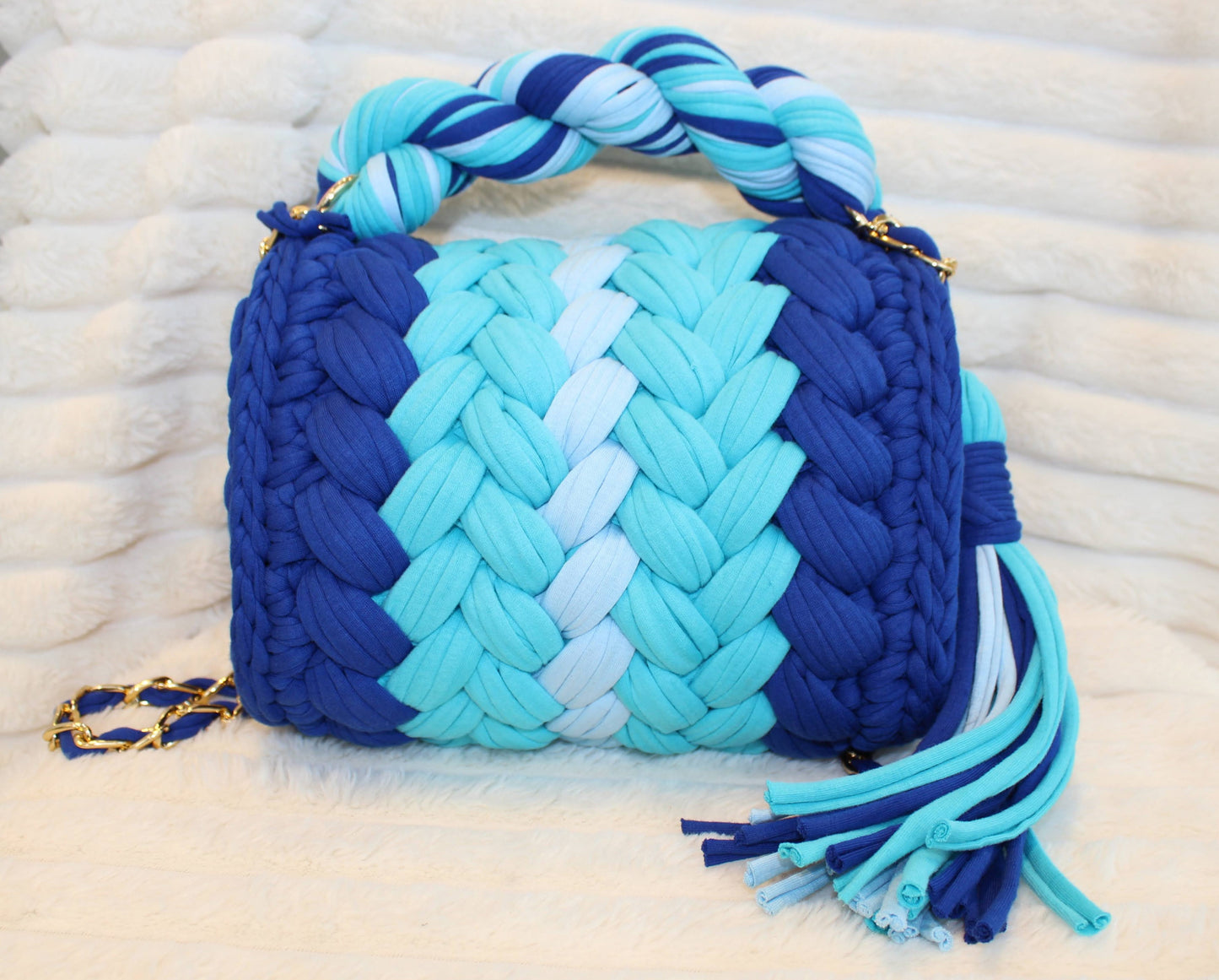 Back view of bag in natural lighting: Woven Crochet handbag (Royal Blue, Light Blue, and Ice Blue) with tassel sitting on a white, textured surface. 