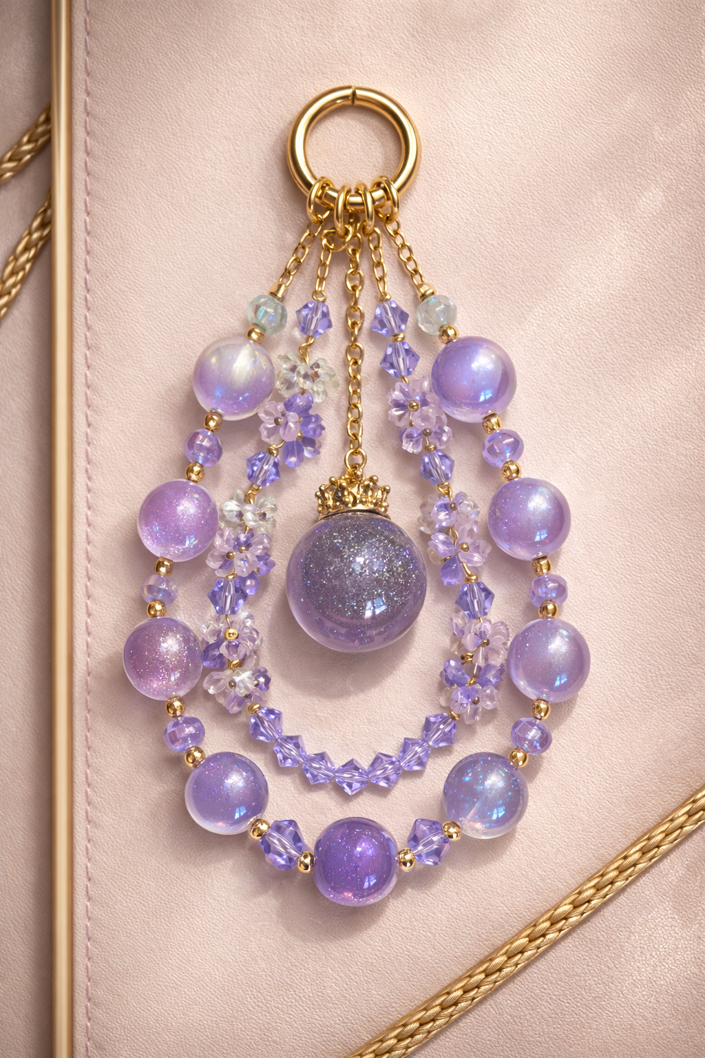 Decorative keychain with soft, pastel lilac beads on a soft, beige background with gold trim. 