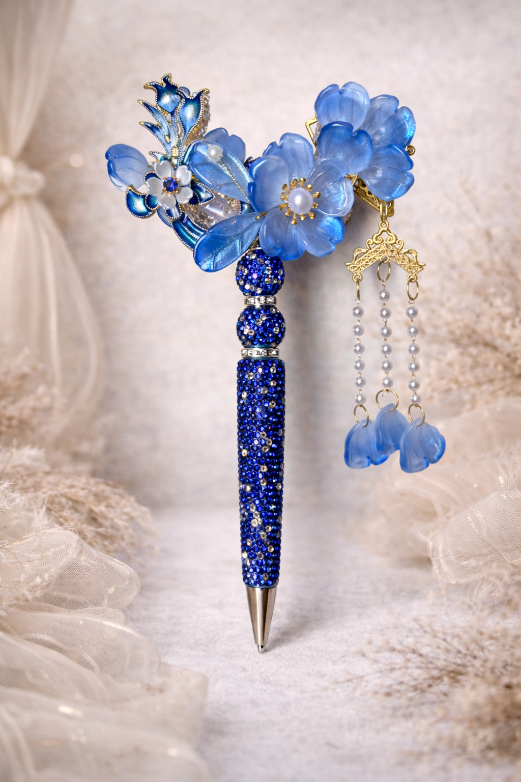 Decorative double-sided royal blue bling pen with a large flower, smaller flower accents, shiny embellishments on a linen and lace background. 