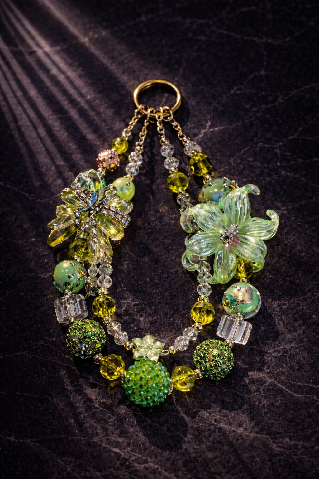 Decorative keychain in many shades of green, with large flower bead, a large green bow, and sparkling beads on a dark marble background