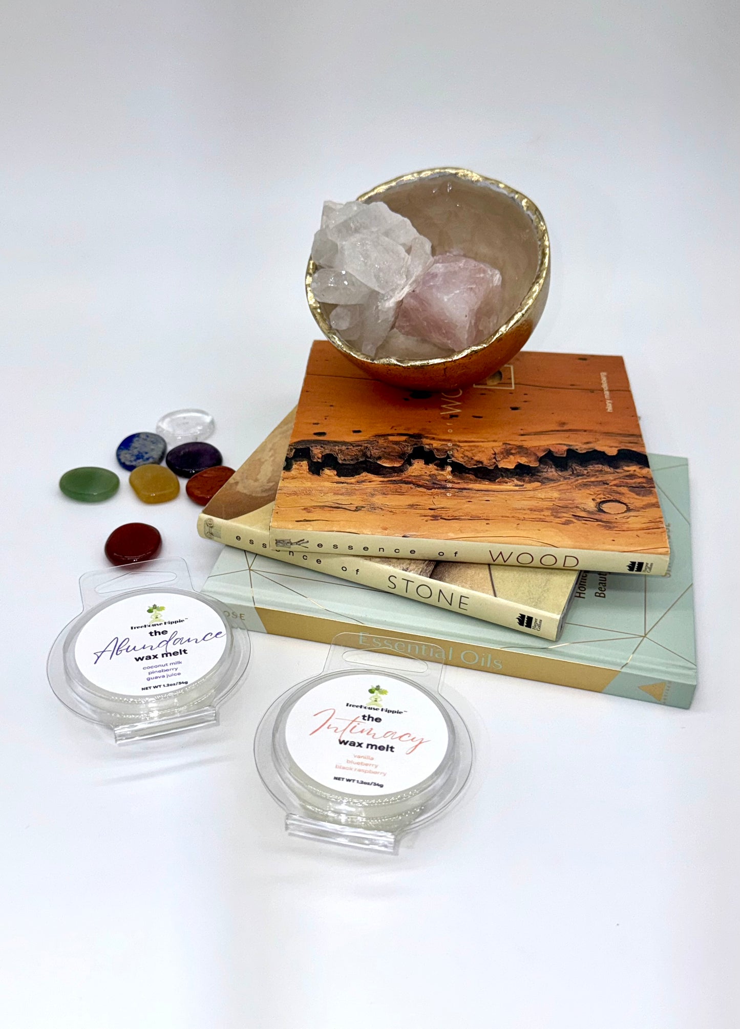 Two wax melts on a white surface with books, a crystal bowl, and stones in the background.