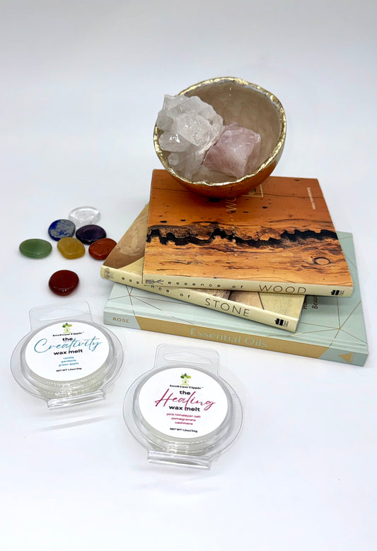 Two wax melts on a white surface with books, a crystal bowl, and stones in the background.