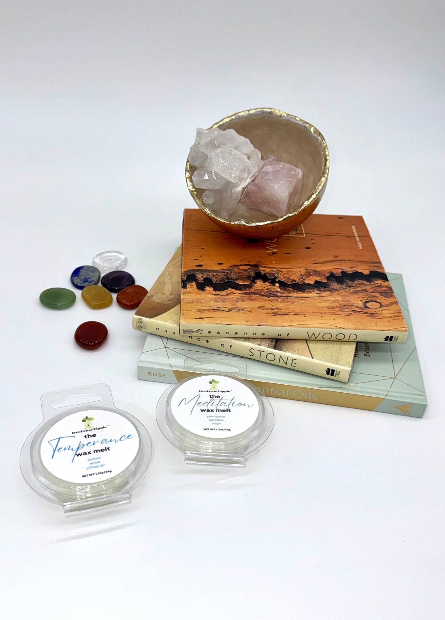 Two wax melts on a white surface with books, a crystal bowl, and stones in the background.