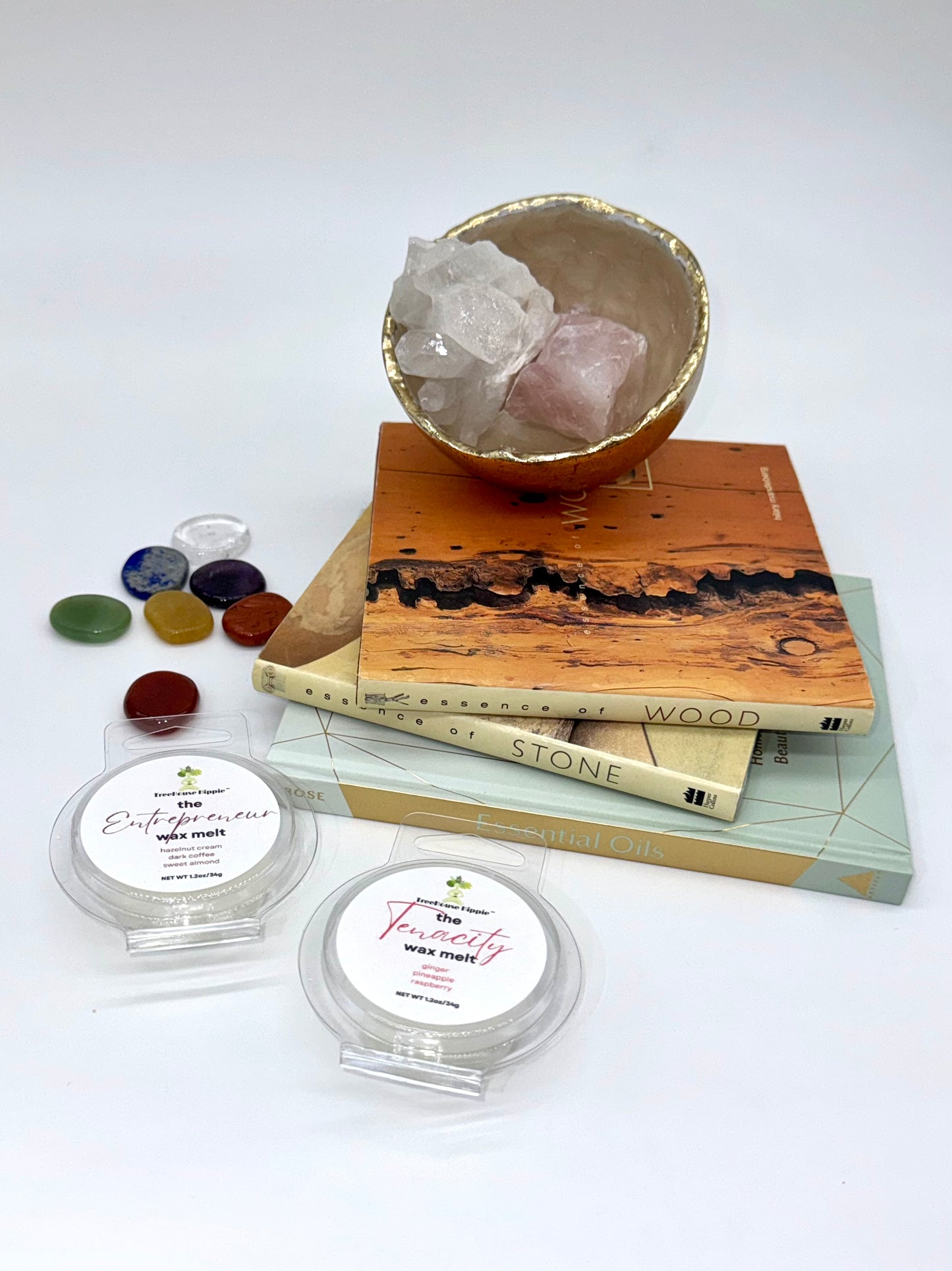 Two wax melts on a white surface with books, a crystal bowl, and stones in the background.