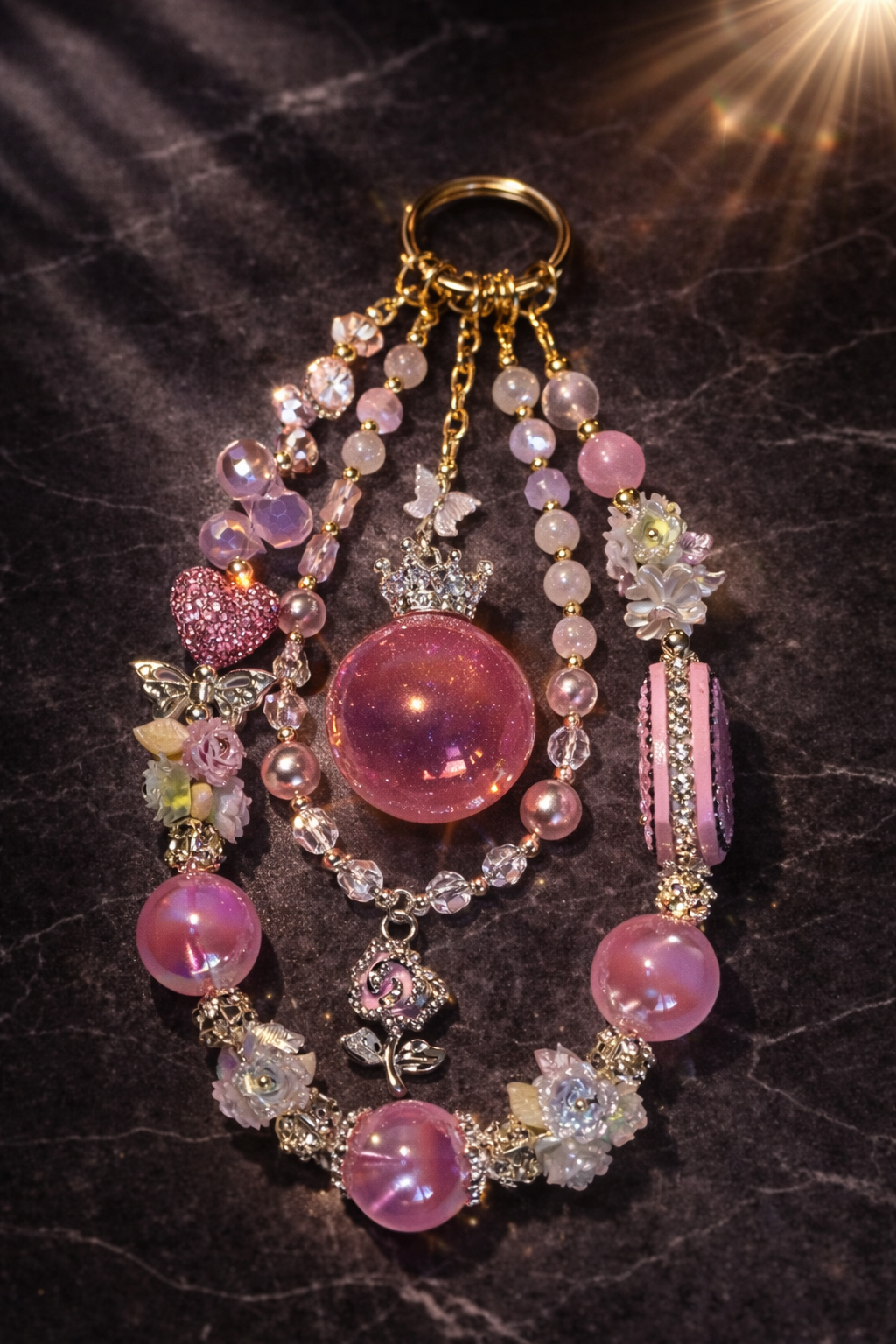 Decorative pink keychain with shimmering pink glass beads, heart and flower charms, and a diamond pink flower pendant on a dark marble background