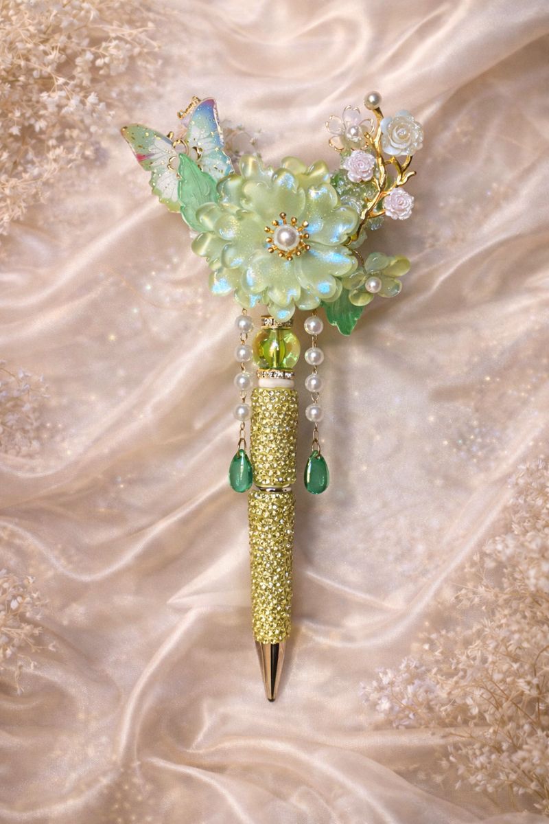 Decorative double-sided mint green bling pen with a large flower, a butterfly charm, floral accents, and green embellishments on a soft silky background