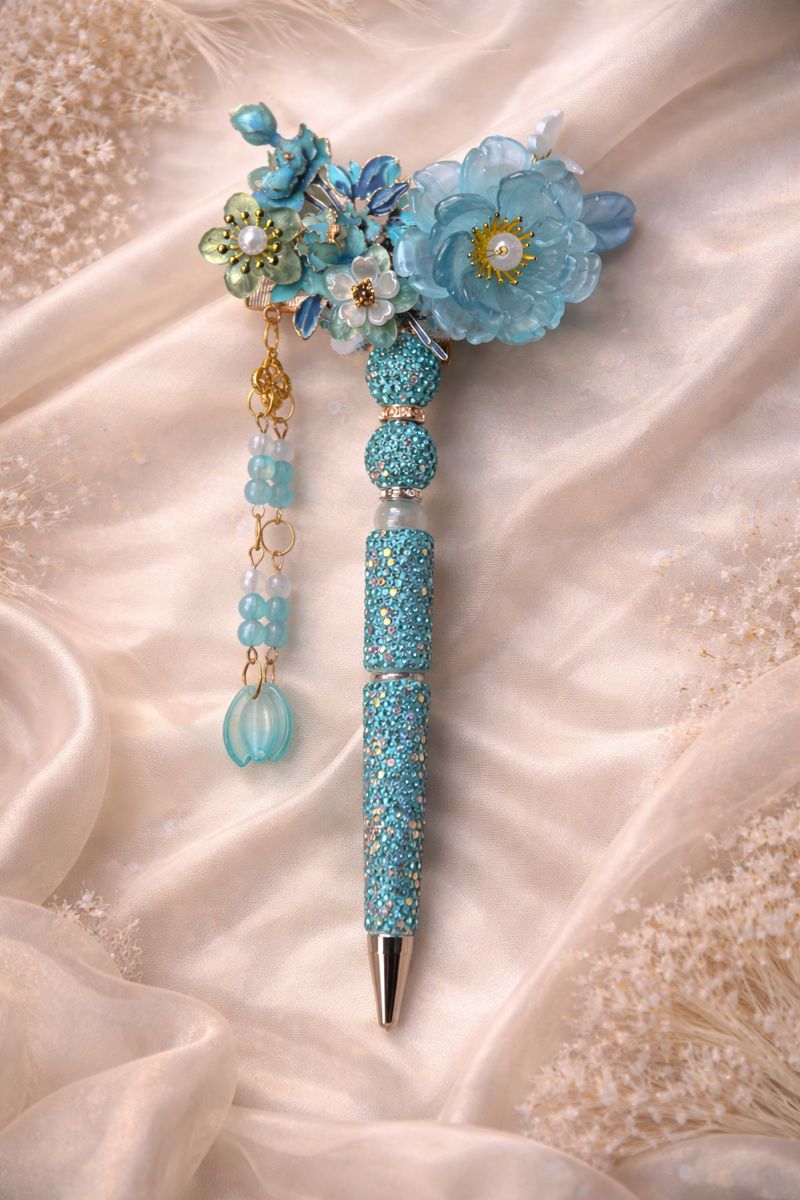 Decorative double-sided baby blue bling pen with a large flower, smaller flower accents, shiny embellishments on a soft silky background. 