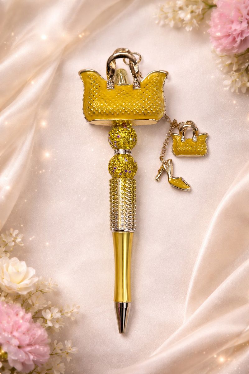 Yellow bling pen with purse charm decorative top on a soft fabric background with flowers