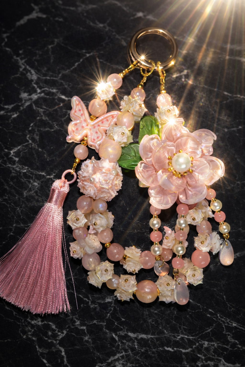 Decorative pink keychain with a large pink flower charm, light pink shimmering beads, floral accents, and a rose pink tassel on a dark marble background