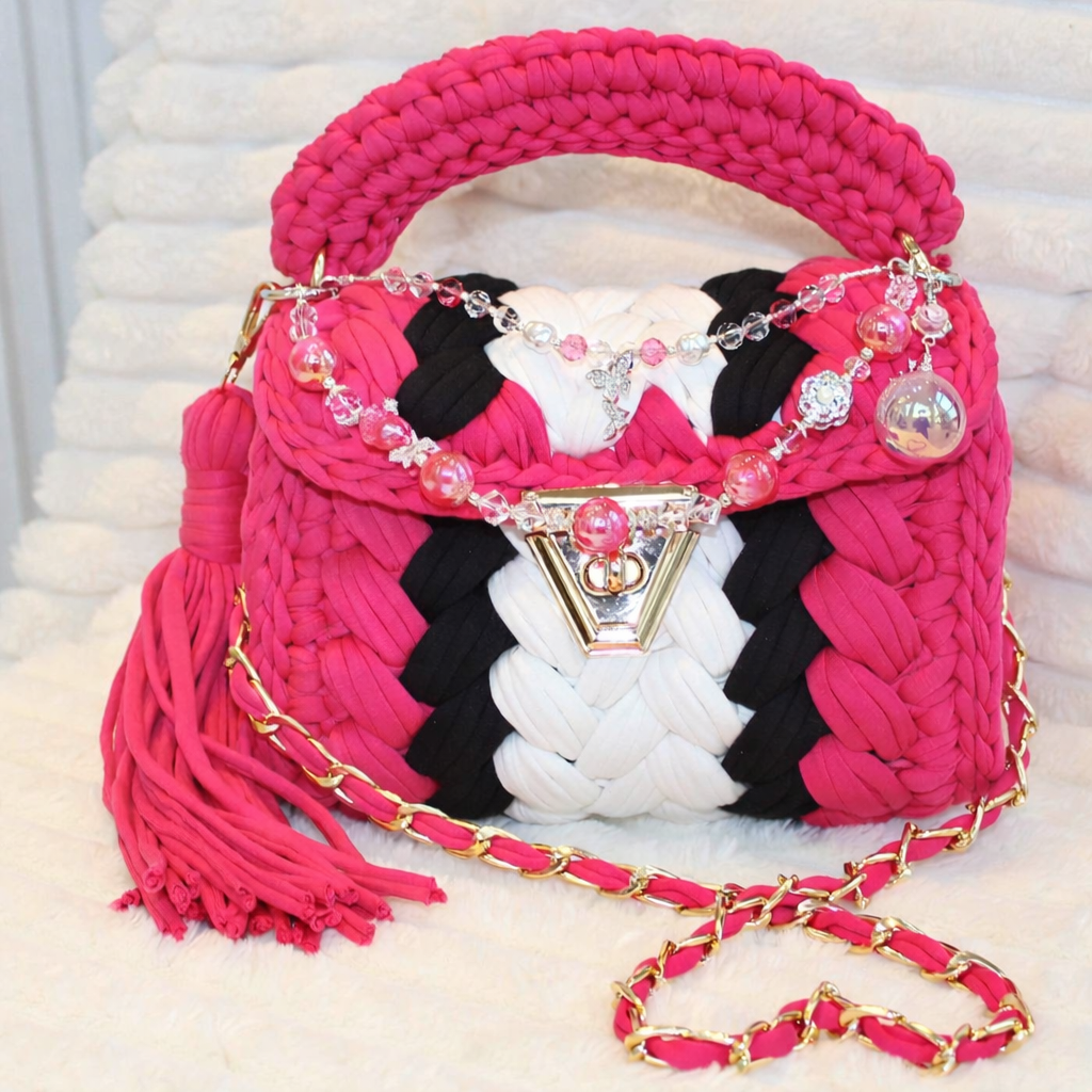 Front of the Bag in natural lighting: Hot Pink, White, and Black Crochet woven handbag with decorative keychain and Hot Pink tassel sitting on a White textured background