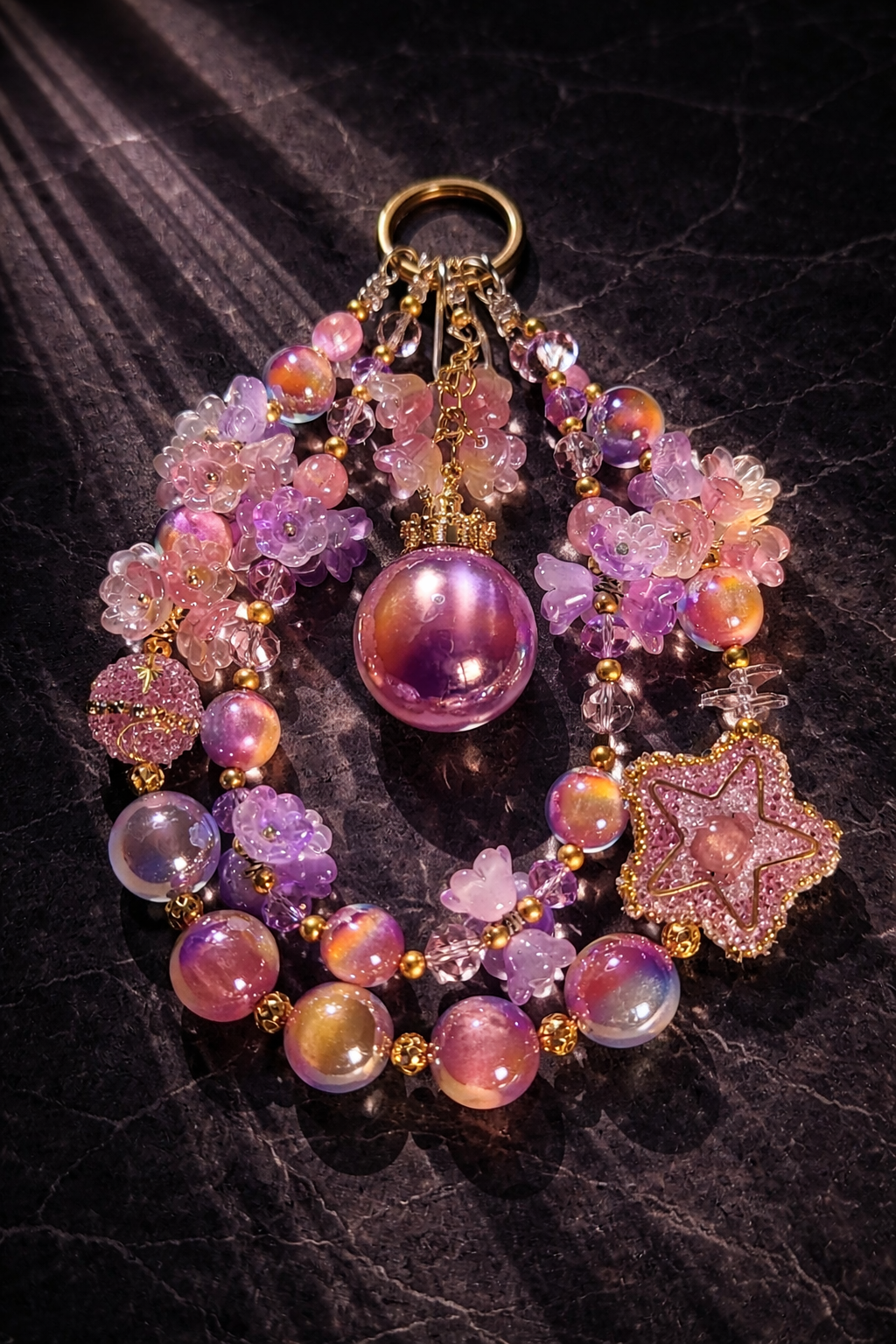 Large decorative gold, peach, orange, and purple keychain with shimmering beads, a large star charm covered in crystal beads, and flower accents on a dark textured marble background. 